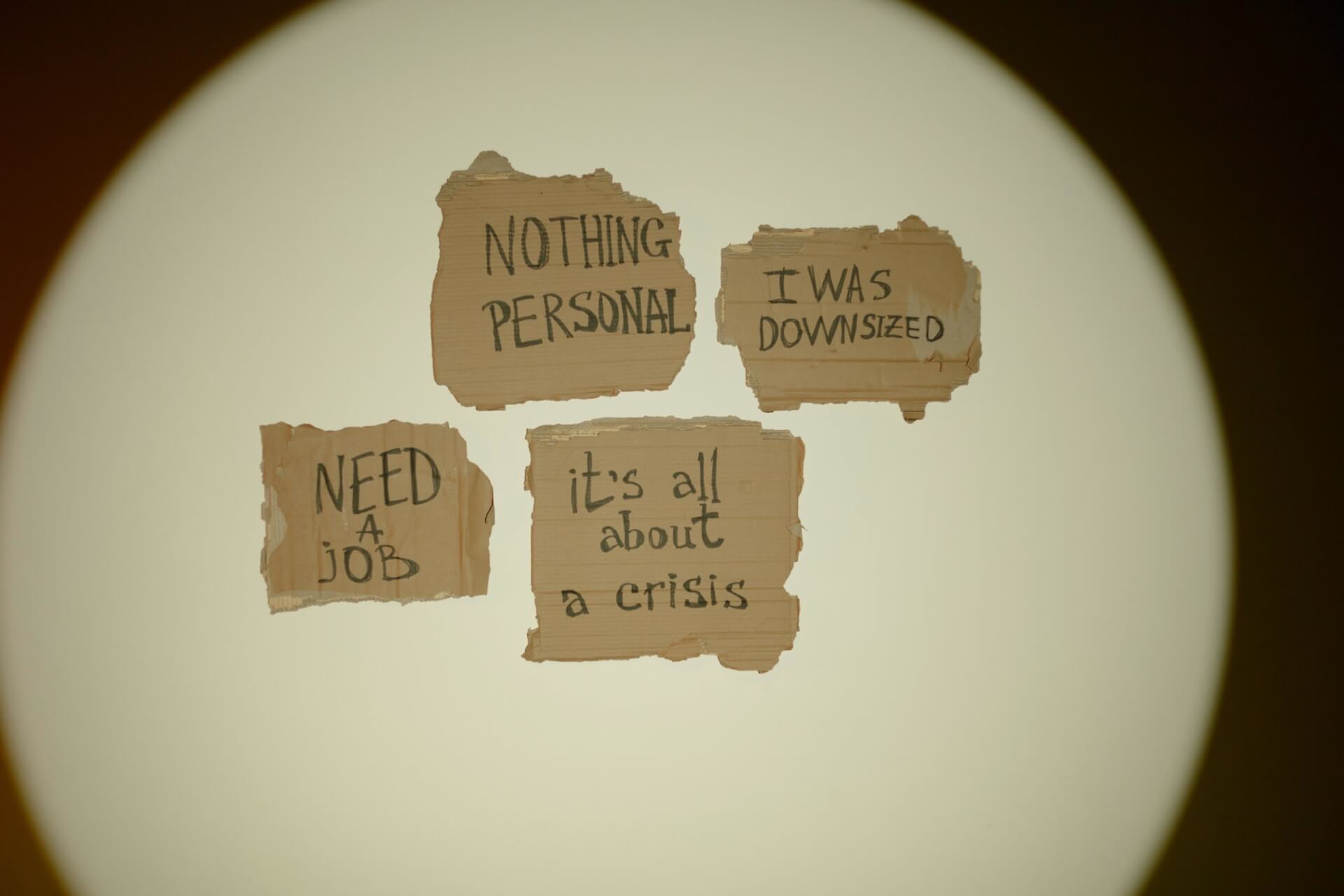 Photo de bouts de papier d&eacute;chir&eacute;s accroch&eacute;s sur le mur sur lesquels sont &eacute;crits &agrave; la main "need a job" "nothing personnal" "it's all about crisis"